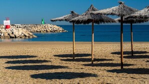 A beach with thatched umbrellas, a rocky breakwater, and a lighthouse. - Belvilla by OYO Apartamento Port Avenue (Marbella)