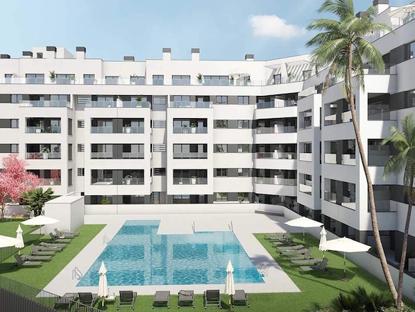 A modern multi-story hotel with a central swimming pool surrounded by lounge chairs and umbrellas, and a palm tree on the right.