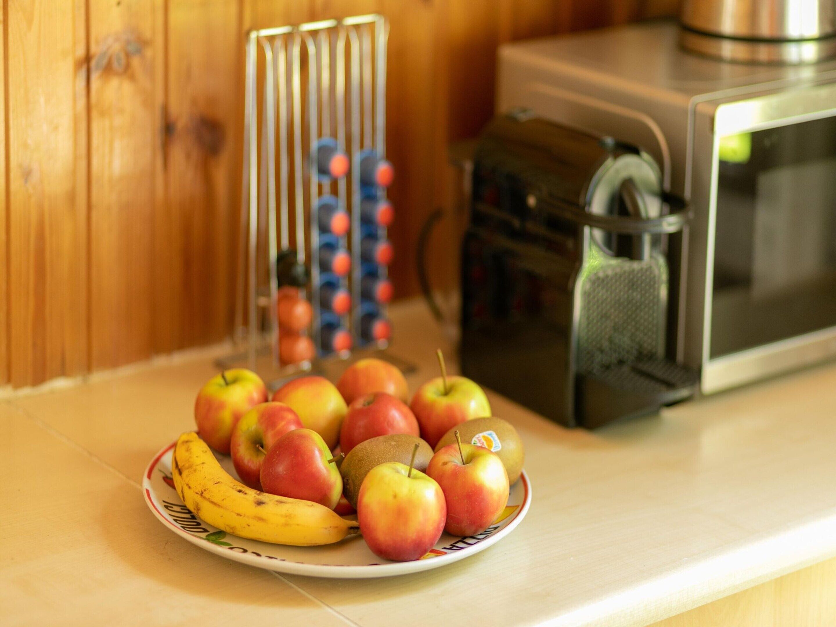 A plate of apples and a banana on a kitchen counter with a microwave in the background.