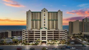 A multi-story hotel with a central entrance, parking garage, and a view of the ocean at sunset. - Luxury Oceanfront 3Bedroom Paradise (North Myrtle Beach)