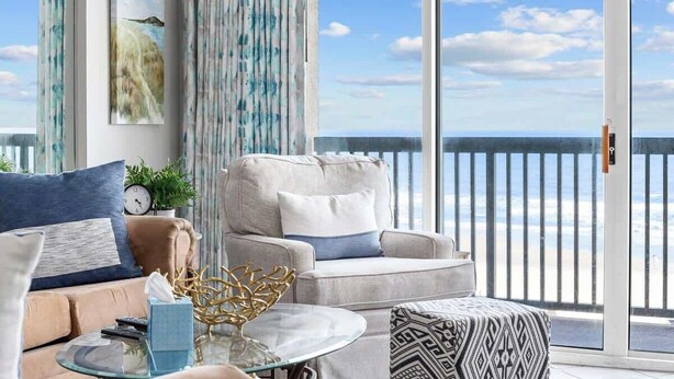 A balcony with a view of the sea, a sofa, a coffee table, and a patterned ottoman. - Luxury Oceanfront 3Bedroom Paradise (North Myrtle Beach)