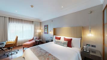 Quarto de hotel com uma cama grande, uma escrivaninha, uma cadeira, um abajur e uma mesa de cabeceira.