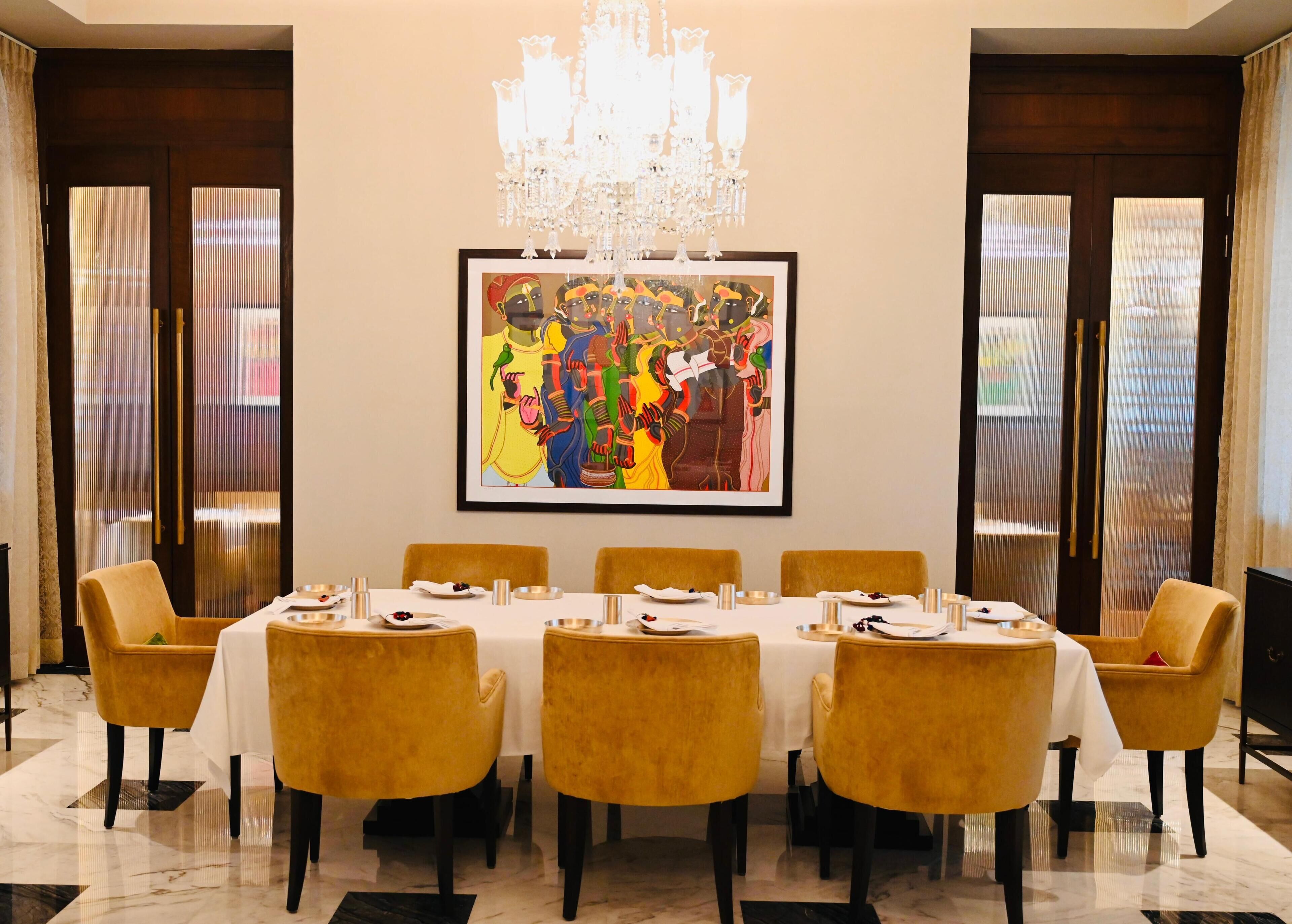 Comedor con una larga mesa dispuesta para ocho personas, rodeada de sillas amarillas, un candelabro y un cuadro abstracto enmarcado en la pared.