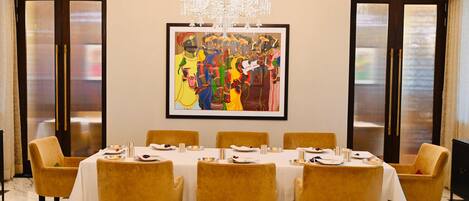 Comedor con una larga mesa dispuesta para ocho personas, rodeada de sillas amarillas, un candelabro y un cuadro abstracto enmarcado en la pared.