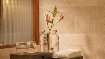 Un baño moderno con un espejo grande, una lámpara fijada a la pared, un jarrón con una flor rosa y artículos de tocador ordenados.