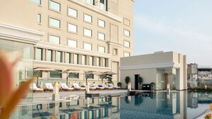 A modern hotel with a rooftop infinity pool, sun loungers, and a glass-enclosed lounge area.