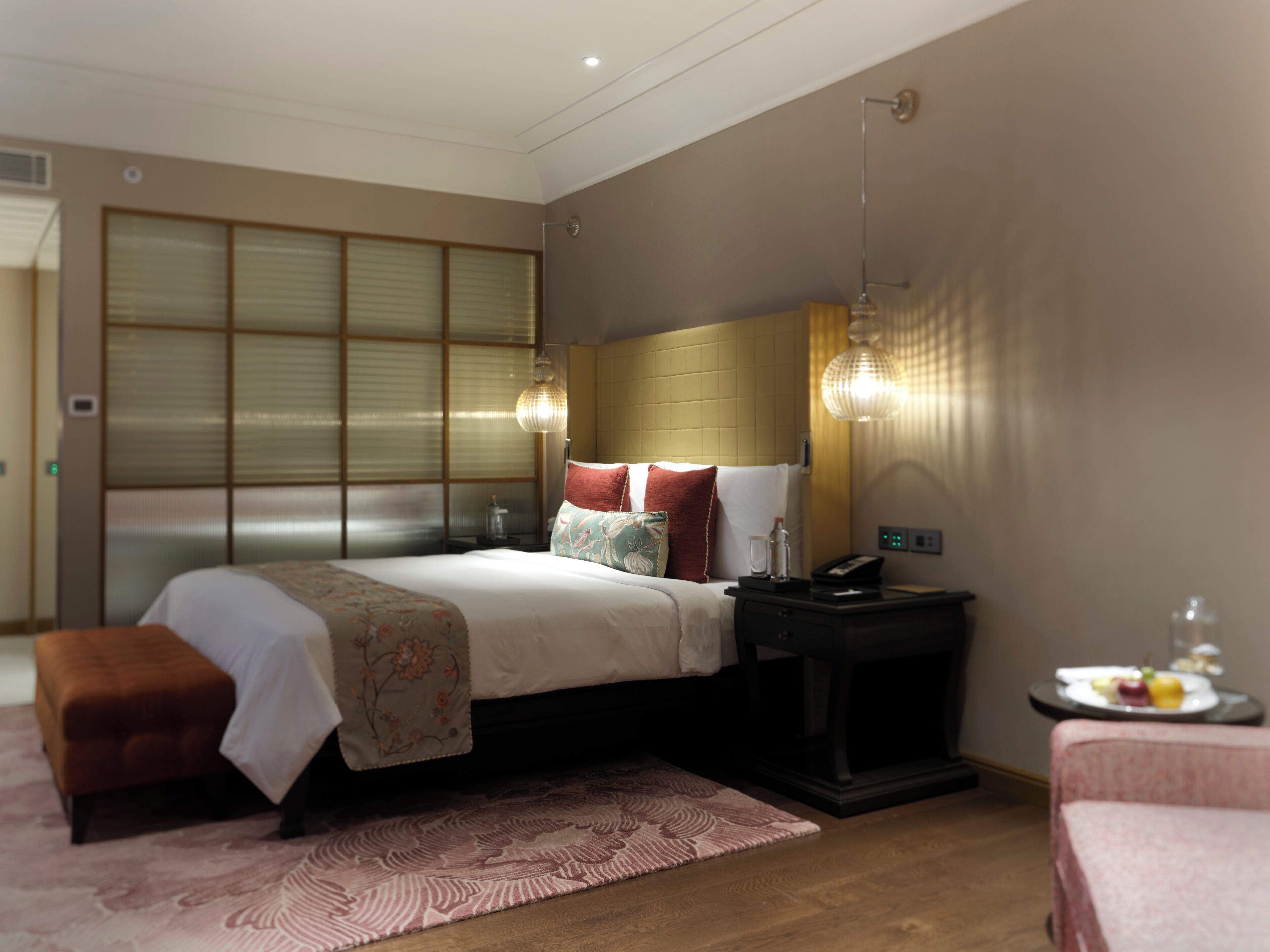 A modern hotel room with a large bed, bedside tables, a small table with fruit, and a traditional sliding door.