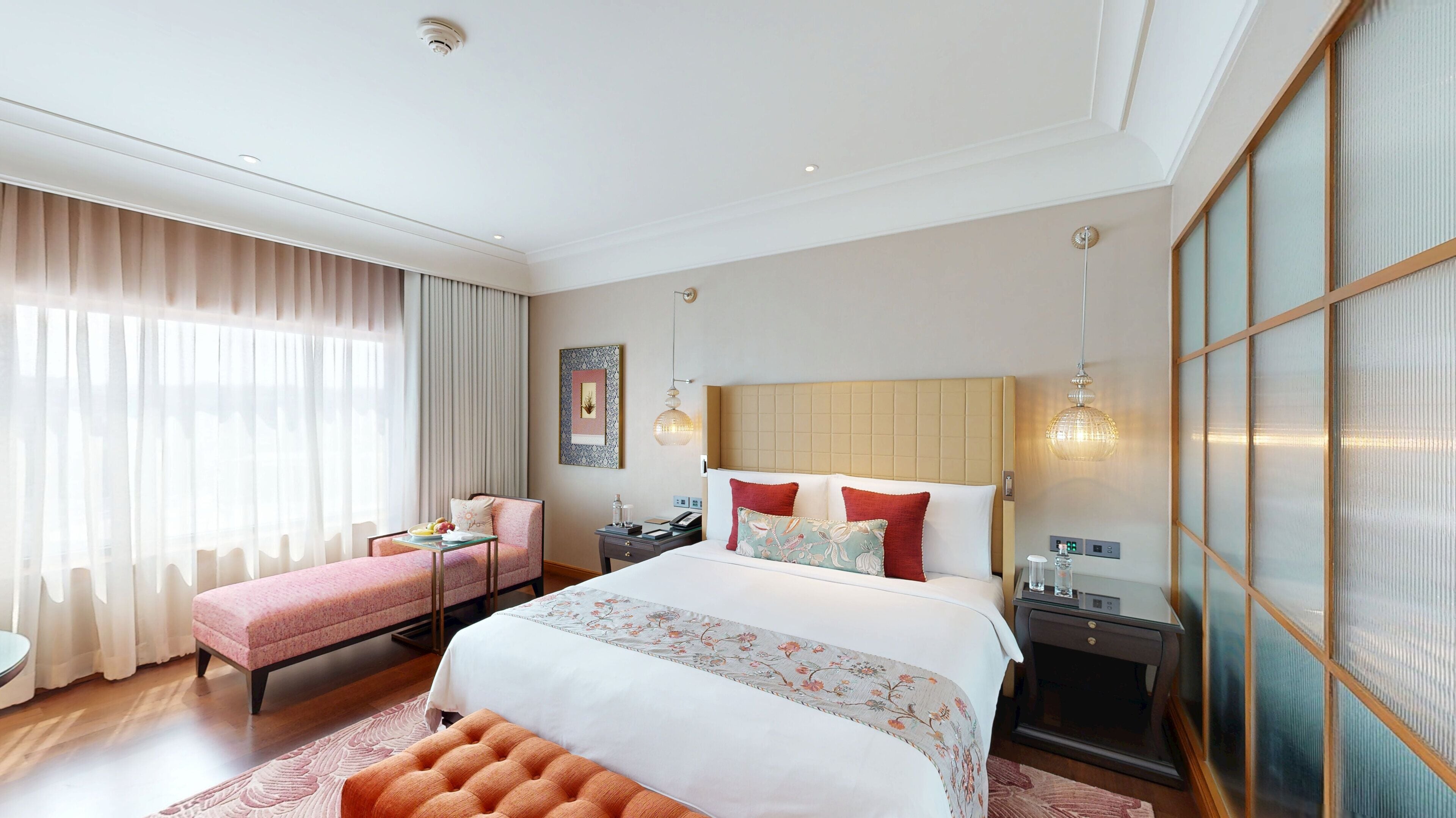 Een hotelkamer met een groot bed, een bureau, een stoel en een bank. Er is een raam met gordijnen en een wandlamp.