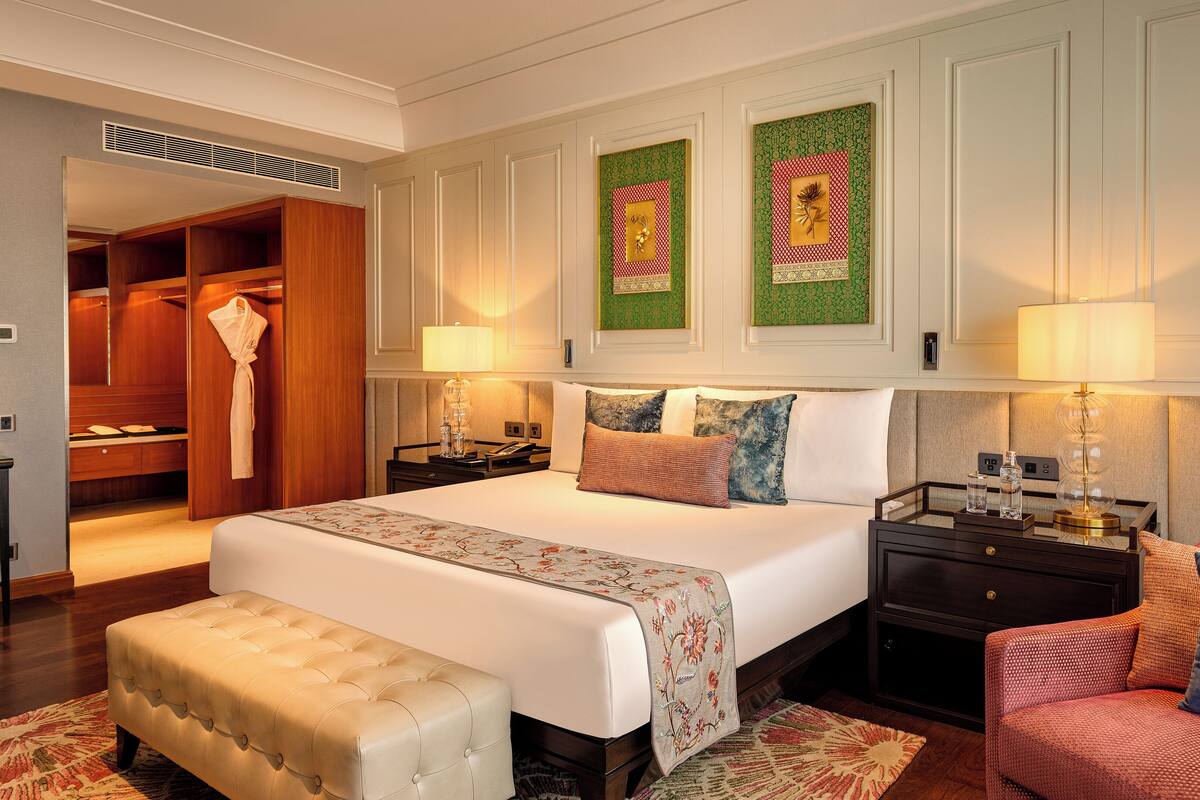 Habitación de hotel con una cama grande, un área de descanso con un banco, una tocador con espejo y un vestidor.