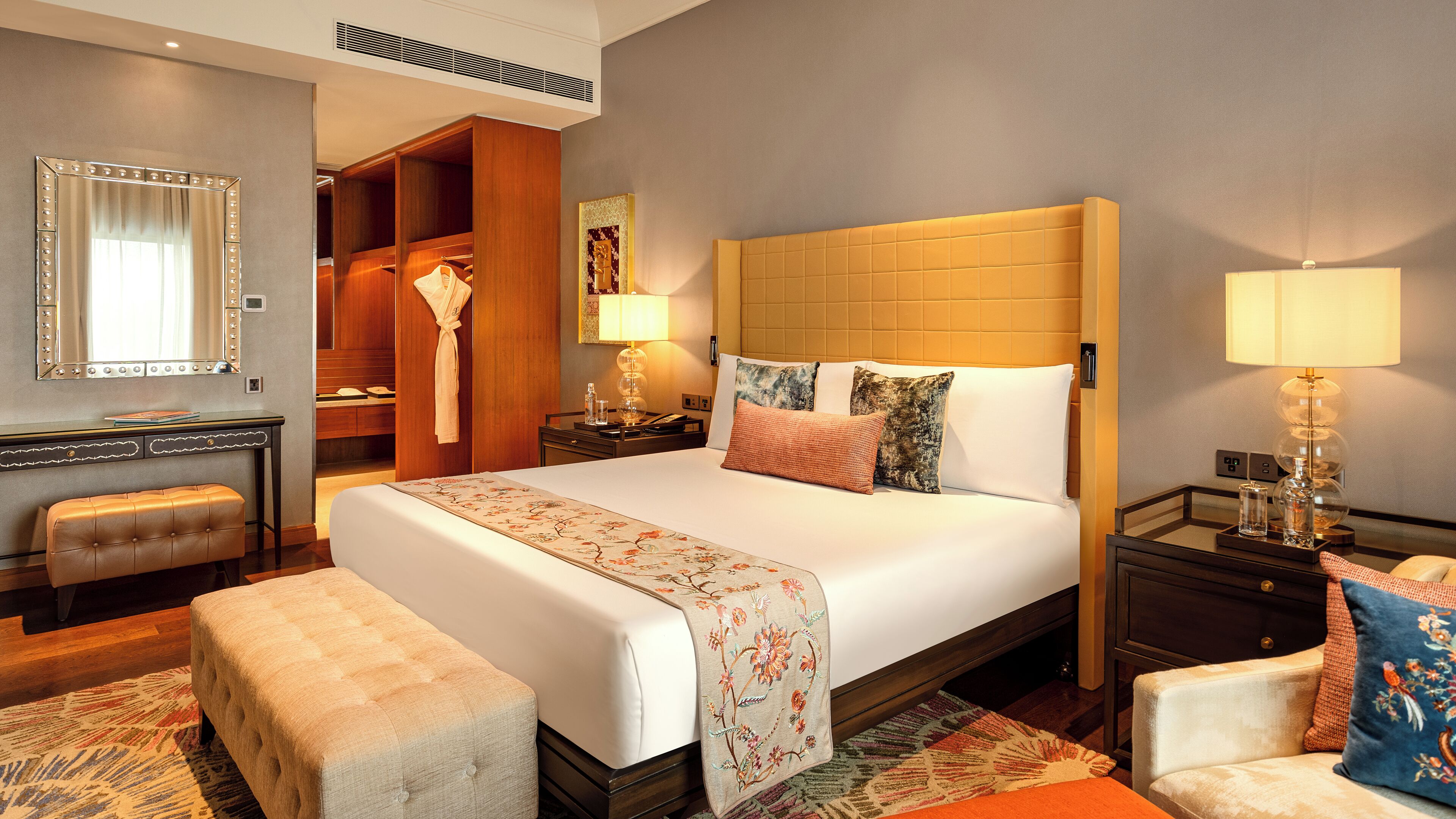 A hotel room with a large bed, a vanity with a mirror, a robe, a desk, and a chair.