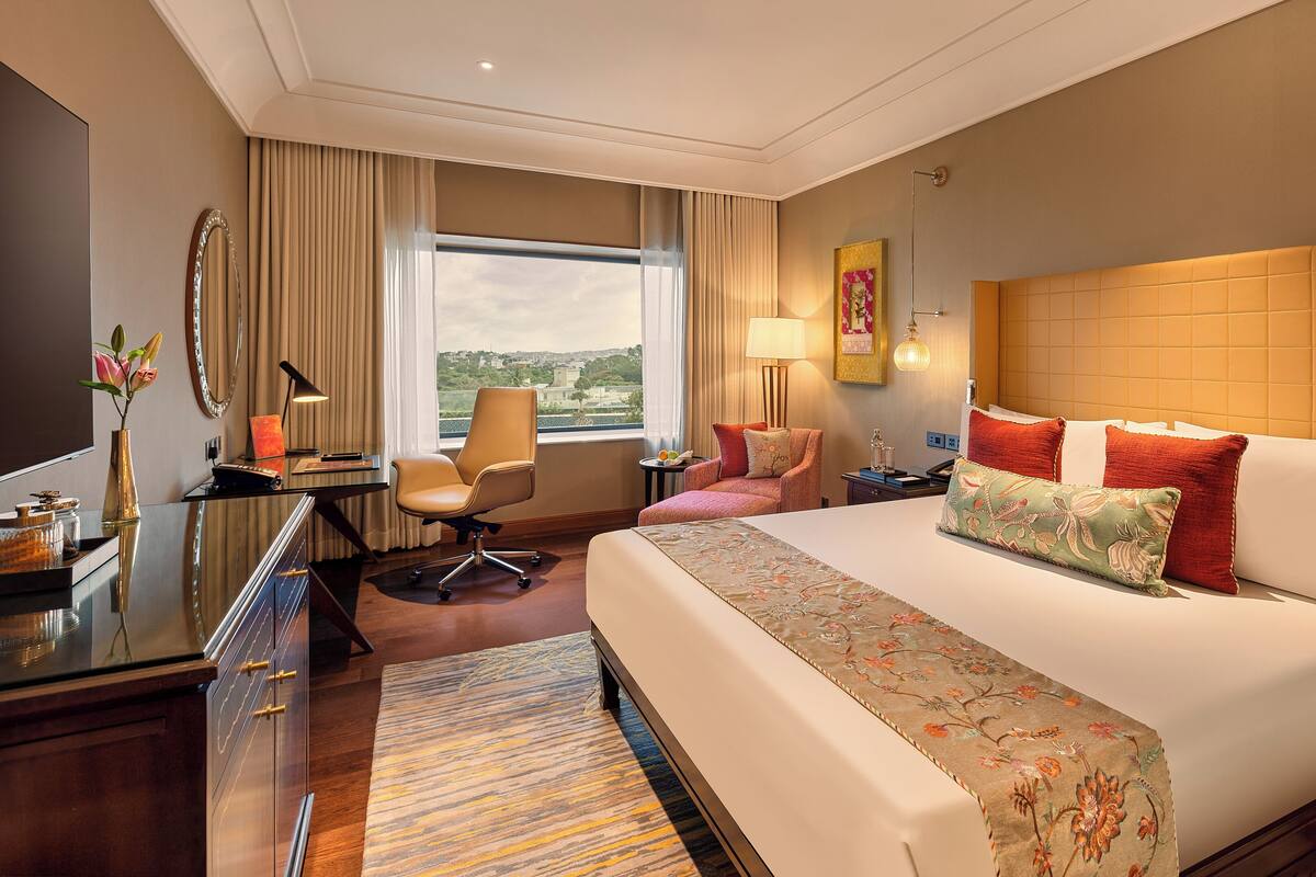Habitación de hotel con una cama grande, un escritorio con silla, televisor y vistas a la ciudad.