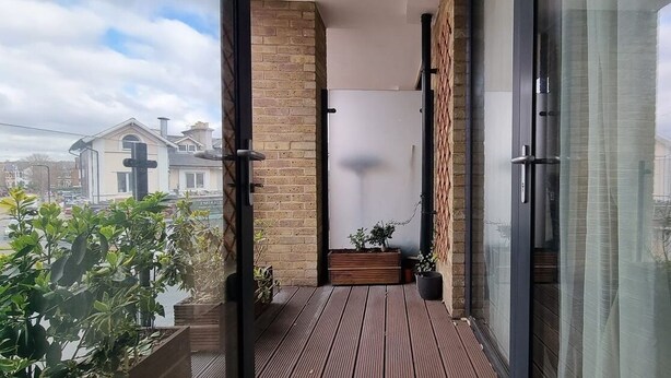 Ein Balkon mit Holzboden, einer Ziegelwand und einer Glastür zu einem Zimmer.