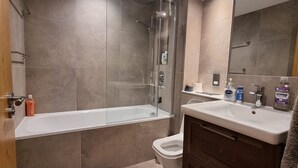 Ein modernes Badezimmer mit einer gläsernen Duschkabine, einer weißen Badewanne und einem Waschtisch mit Spüle und Spiegel.