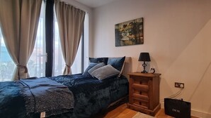 Ein Schlafzimmer mit Bett, Nachttisch, Lampe, einem Bild an der Wand und einem Fenster mit Vorhängen.