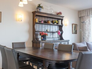 Een eetgedeelte met een houten tafel en stoelen, een decor kast met planken en wandlampen.