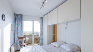 A bedroom with a bed, a chair, a window with curtains, and a view of the outdoors. - Bright Apartment on the 7th Floor (Middelkerke)