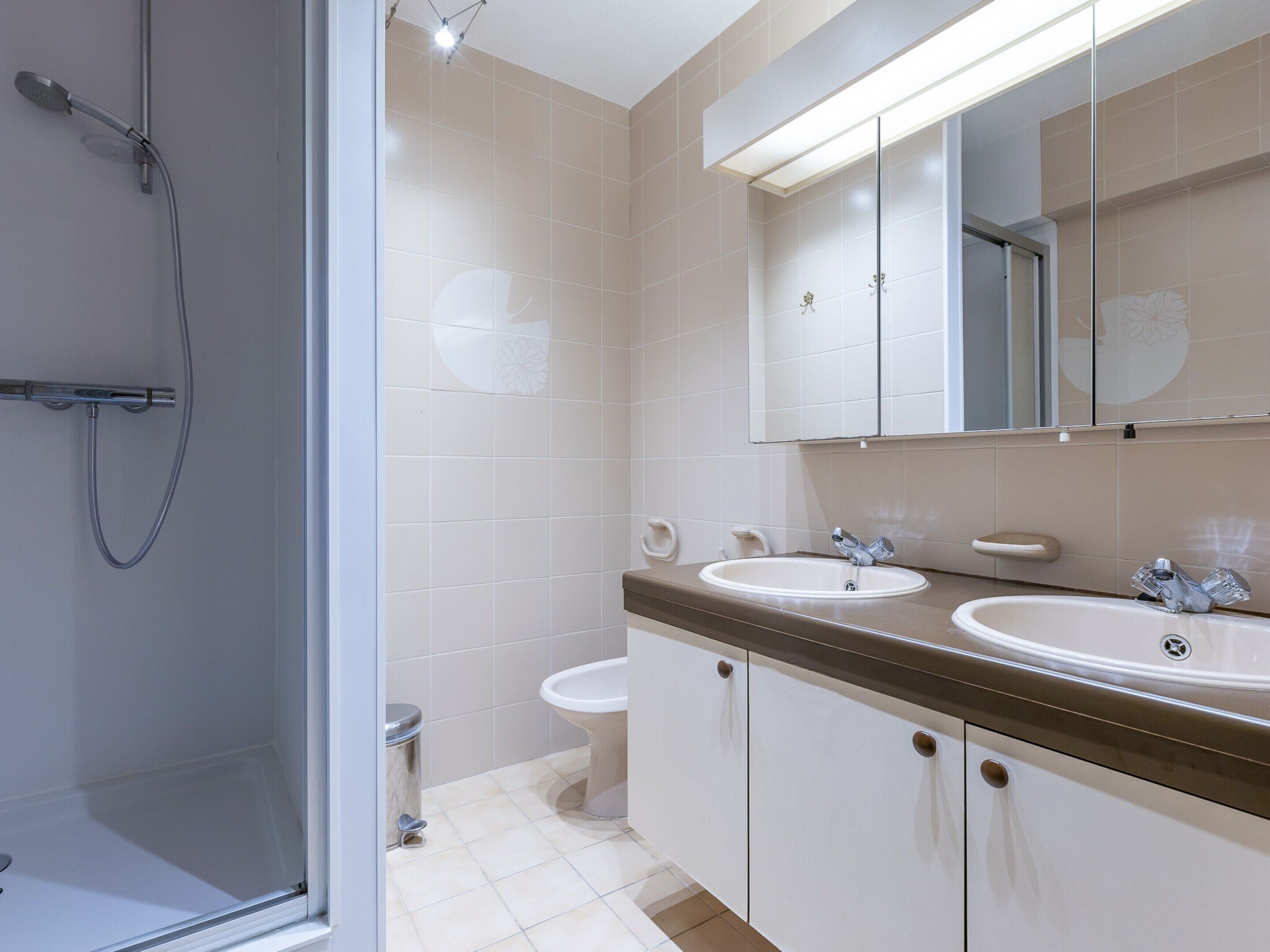 A modern bathroom with a shower, two sinks, a toilet, and a large mirror.