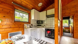 Interior de una cabaña de madera con comedor, kitchenette y vistas al exterior.
