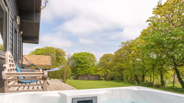 Un jacuzzi con terraza de madera y una hamaca, rodeado de un exuberante jardín y árboles.