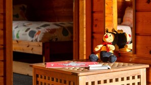 A wooden cabin room with a bed, a small table with a stuffed toy and a book, and a wooden door. - Lodge 6 - Hot Tub Lodge by Interhome (Launceston)