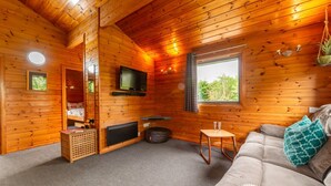 A cozy cabin interior with a wooden ceiling, a television mounted on the wall, a sofa with cushions, and a window providing a view of the outdoors. - Lodge 6 - Hot Tub Lodge by Interhome (Launceston)