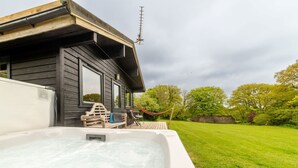 A hot tub with a wooden deck and a hammock, a wooden house with a window, and a grassy yard with trees. - Lodge 6 - Hot Tub Lodge by Interhome (Launceston)