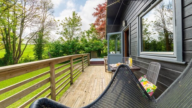 A wooden deck with a wicker chair and a table, overlooking a green landscape. - Lodge 4 Hot Tub by Interhome (Launceston)