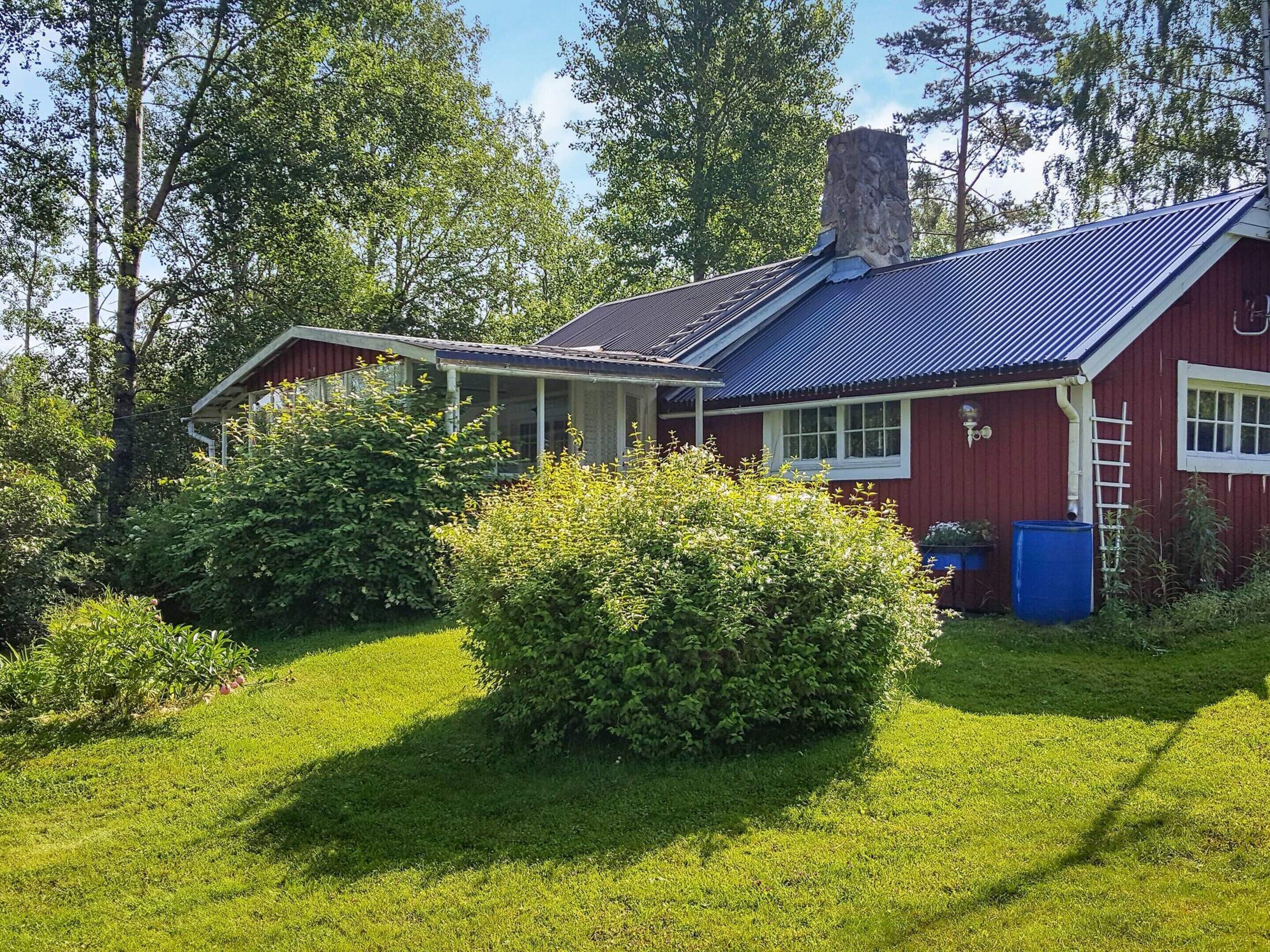 A red house with a blue roof, surrounded by green grass and trees.
