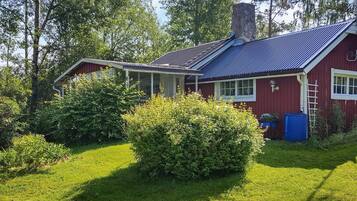 A red house with a blue roof, surrounded by green grass and trees.