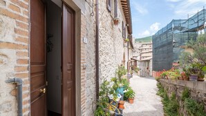 A narrow alleyway with a stone building, wooden doors, and potted plants lining the path. - Belvilla by OYO Casa Castiglia (Polino)