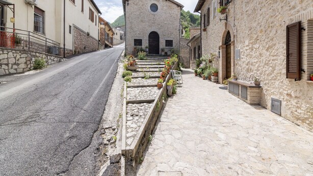 A narrow street with stone buildings, a church with a bell tower, and a row of potted plants along the sidewalk. - Belvilla by OYO Casa Castiglia (Polino)