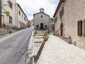 Una calle estrecha con edificios de piedra, una iglesia con campanario y una fila de macetas a lo largo de la acera.