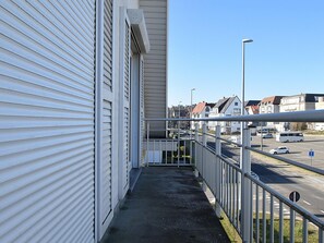 En balkon med gelænder i metal, der ud til en gade med biler og bygninger.