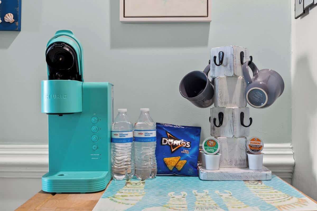 A teal Keurig coffee maker, two water bottles, a bag of Doritos, and a coffee station with Dunkin' Donuts cups.