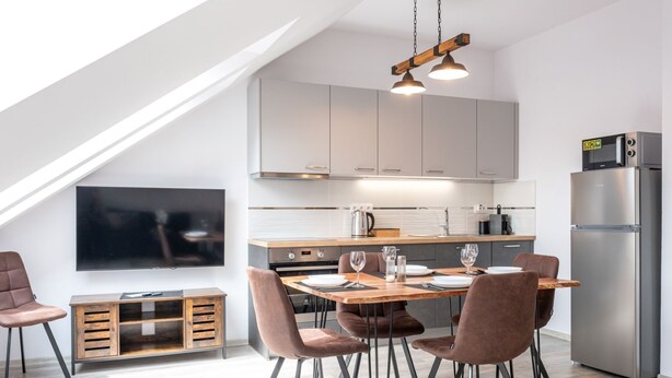 A modern kitchen with a dining area, featuring a wooden table, chairs, and a built-in oven. - Miner's Lodge & Sauna by Interhome (Jachymov)