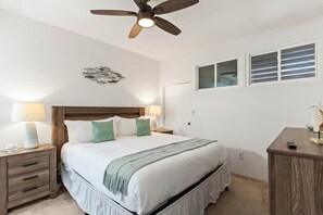 Ein Schlafzimmer mit einem Bett, Nachttischen, einem Schreibtisch, einem Deckenventilator und einem Fenster mit Jalousien.
