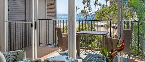 A balcony with a view of the ocean, a table with a vase, and a chair.