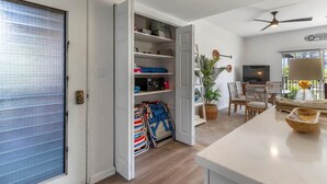 An open closet with shelves, a folded chair, a dining area with a table and chairs, and a ceiling fan. - Dreamy Coastal Retreat (Kihei)