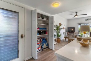 An open closet with shelves, a folded chair, a dining area with a table and chairs, and a ceiling fan. - Dreamy Coastal Retreat (Kihei)