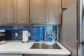 A kitchen with wooden cabinets, a stainless steel sink, and blue-tiled backsplash.