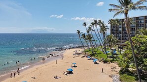 A beach with a hotel building, palm trees, and umbrellas.