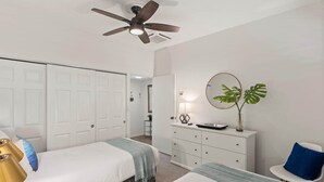 A bedroom with two beds, a ceiling fan, a dresser, a mirror, and a plant. - Dreamy Coastal Retreat (Kihei)