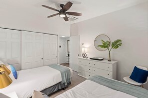 A bedroom with two beds, a ceiling fan, a dresser, a mirror, and a plant. - Dreamy Coastal Retreat (Kihei)