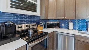 A modern kitchen with stainless steel appliances, wooden cabinets, and blue-tiled backsplash. - Dreamy Coastal Retreat (Kihei)