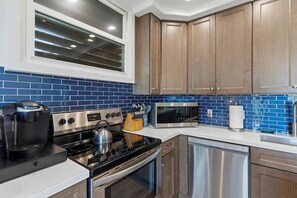 A modern kitchen with stainless steel appliances, wooden cabinets, and blue-tiled backsplash. - Dreamy Coastal Retreat (Kihei)