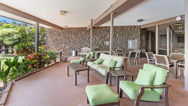 A covered outdoor seating area with stone walls, green cushioned furniture, and a view of the garden. - Dreamy Coastal Retreat (Kihei)