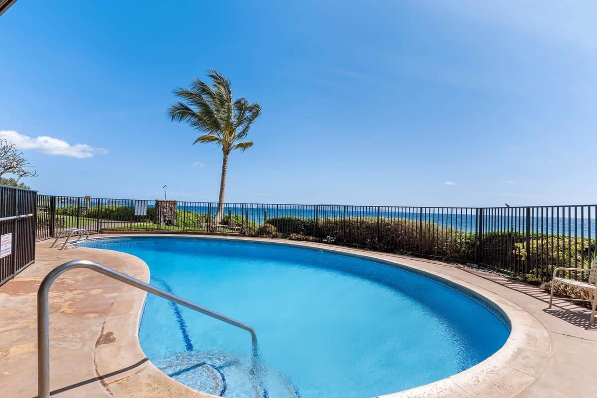 En pool med buet kant, en palme og udsigt til havet.