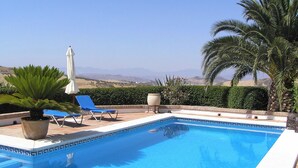 Une piscine aux carreaux bleus, entourée de chaises longues et d’un palmier.