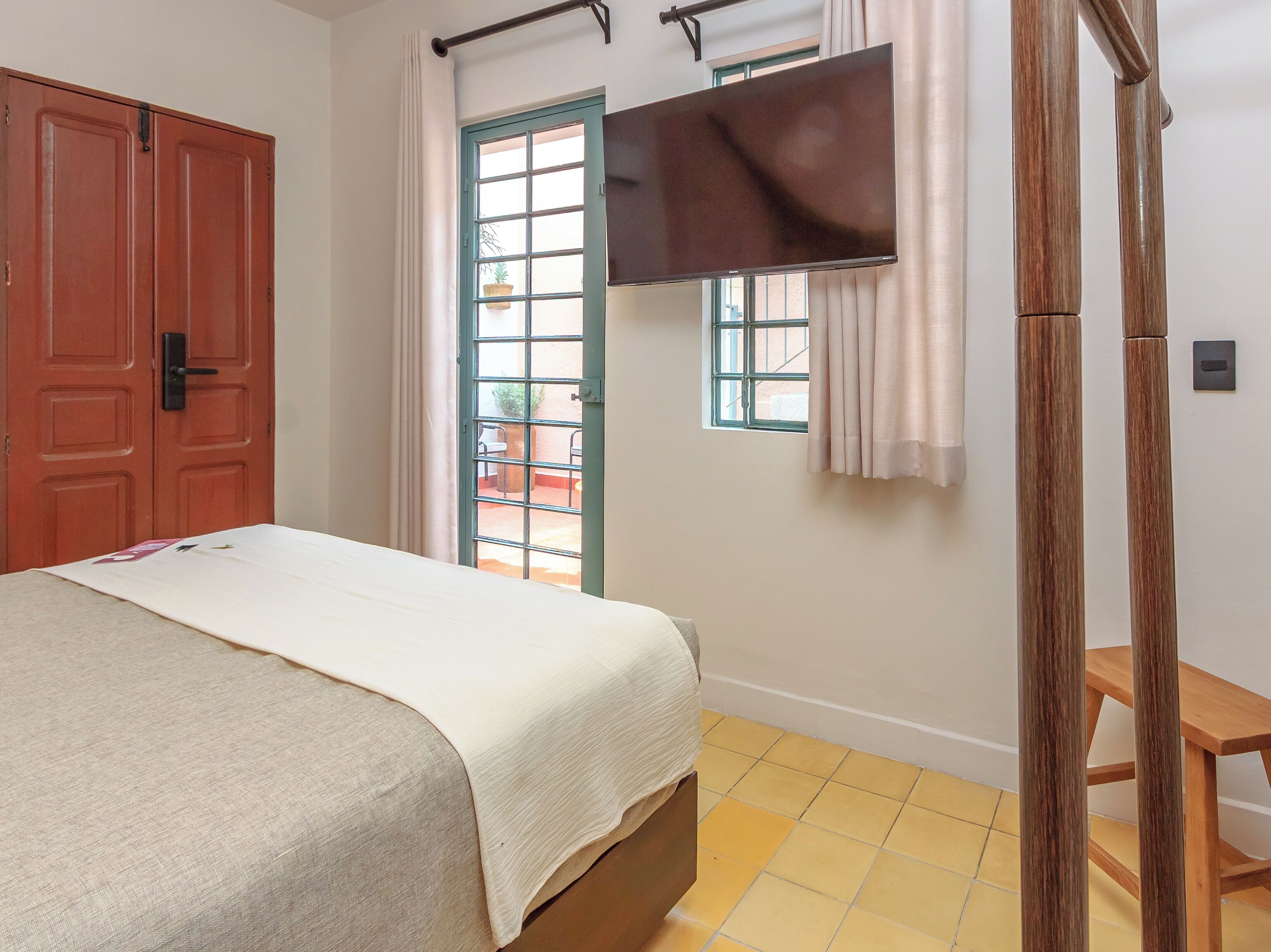 Una camera da letto con un letto, una scrivania in legno, un televisore a parete e una porta con una finestra.