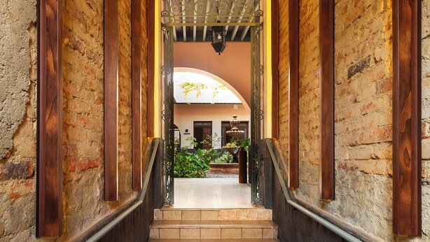 A staircase leading to a courtyard with brick walls, a wooden railing, and a wrought iron gate. - Hotel Libertad 1416 (Guadalajara)